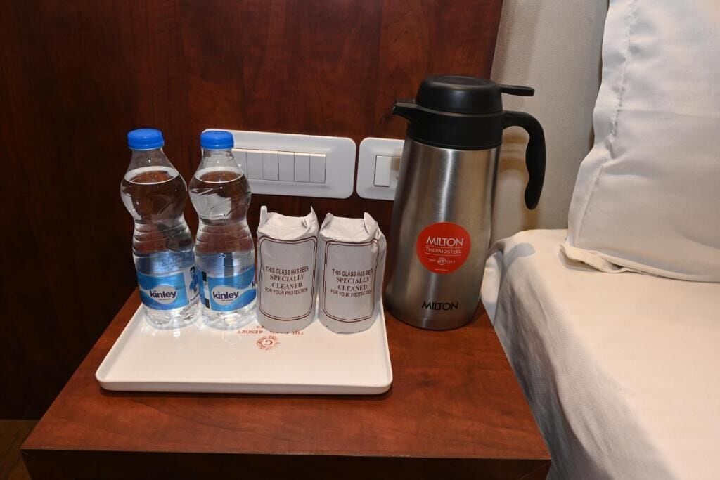 A hotel room with a bedside table holding water bottles, a thermos, and a tray with napkins.