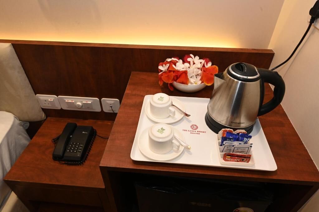 Een hotelkamer met een houten nachtkastje, een telefoon, een dienblad met een koffiezetapparaat, kopjes en een bloemenvaas.