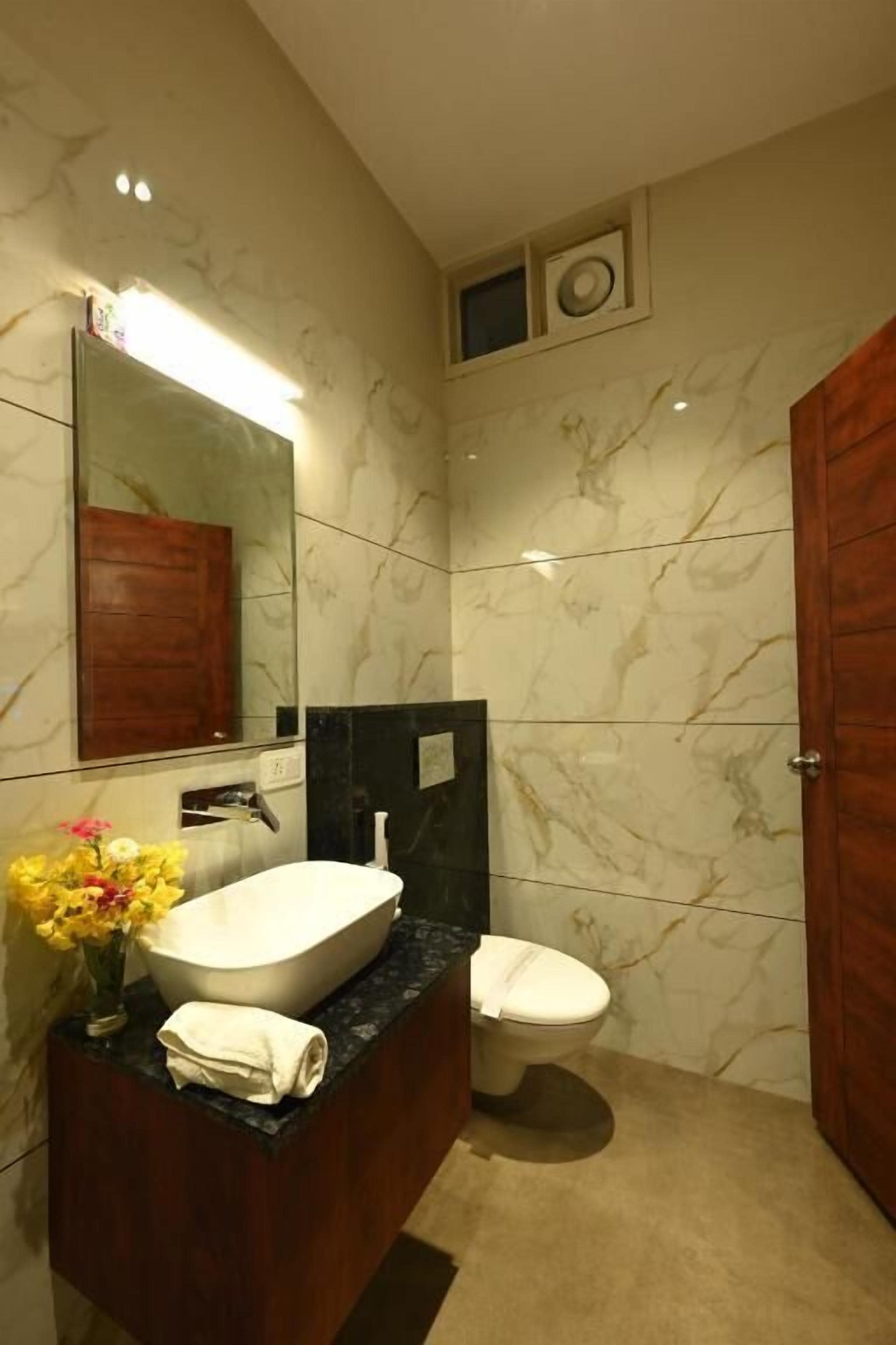 Un bagno con una parete in marmo, un mobile contenitore in legno, un lavabo bianco, un water e uno specchio.