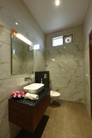 A modern bathroom with marble walls, a large mirror, a white sink, and a toilet.