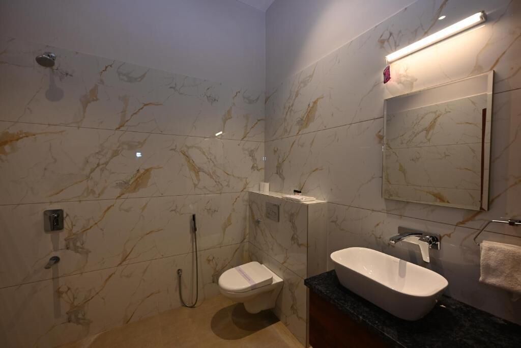 A bathroom with a marble wall, a white toilet, a shower, a sink, and a mirror.