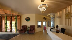 A reception area with a modern design, including a reception desk, two armchairs, a potted plant, and a decorative wall piece. - THE GANGA RESORT (Bikaner)