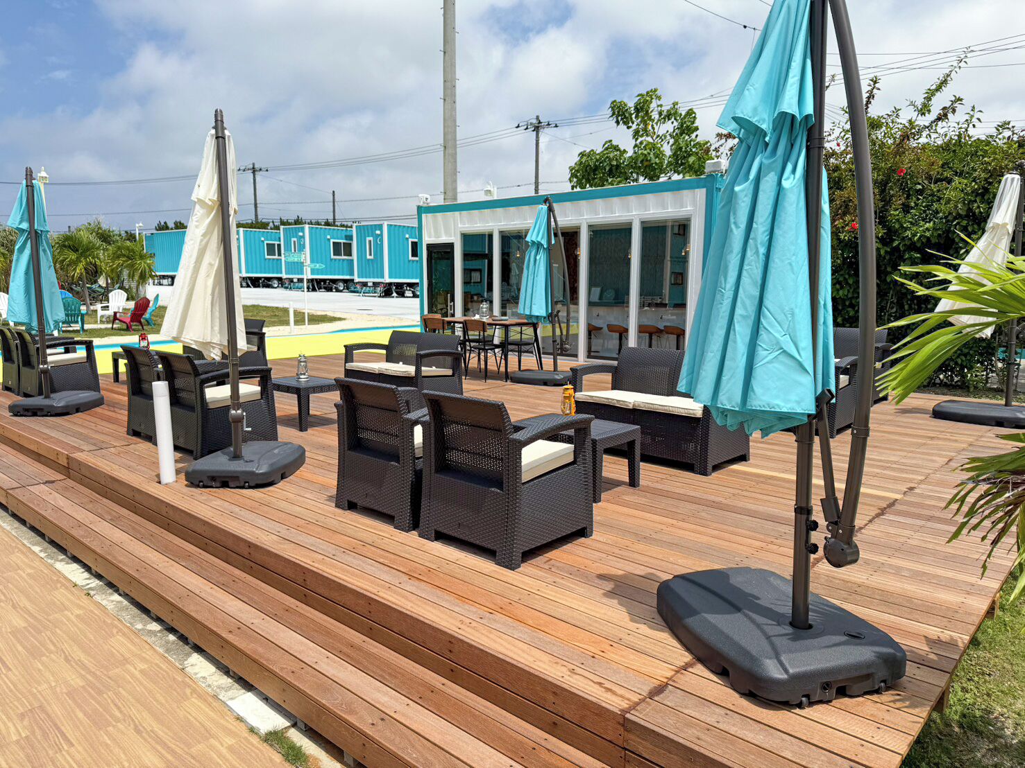 Um deck de madeira com assentos ao ar livre, guarda-sóis e vista para um edifício azul.