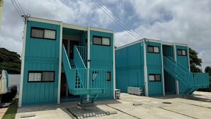 Une rangée de bâtiments modulaires bleus, dotés d’escaliers extérieurs, un sol en béton et un ciel dégagé.