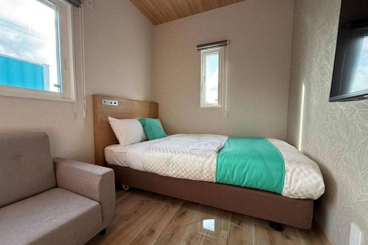 Une pièce de taille modeste comprenant un lit, un canapé, une petite fenêtre et un ventilateur de plafond.