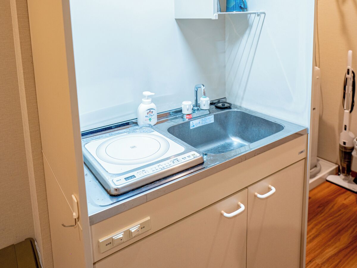 Una kitchenette compacta con una placa vitrocerámica empotrada, un lavamanos y una pequeña encimera.