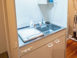 Una kitchenette compacta con una placa vitrocerámica empotrada, un lavamanos y una pequeña encimera.