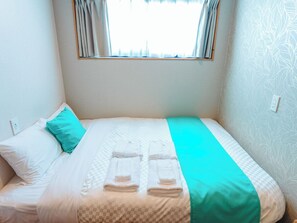 A neatly made bed with a checkered bedspread and two folded towels. - MIYAKOJIMA Blue Village HOTEL & SAUNA (Miyakojima)