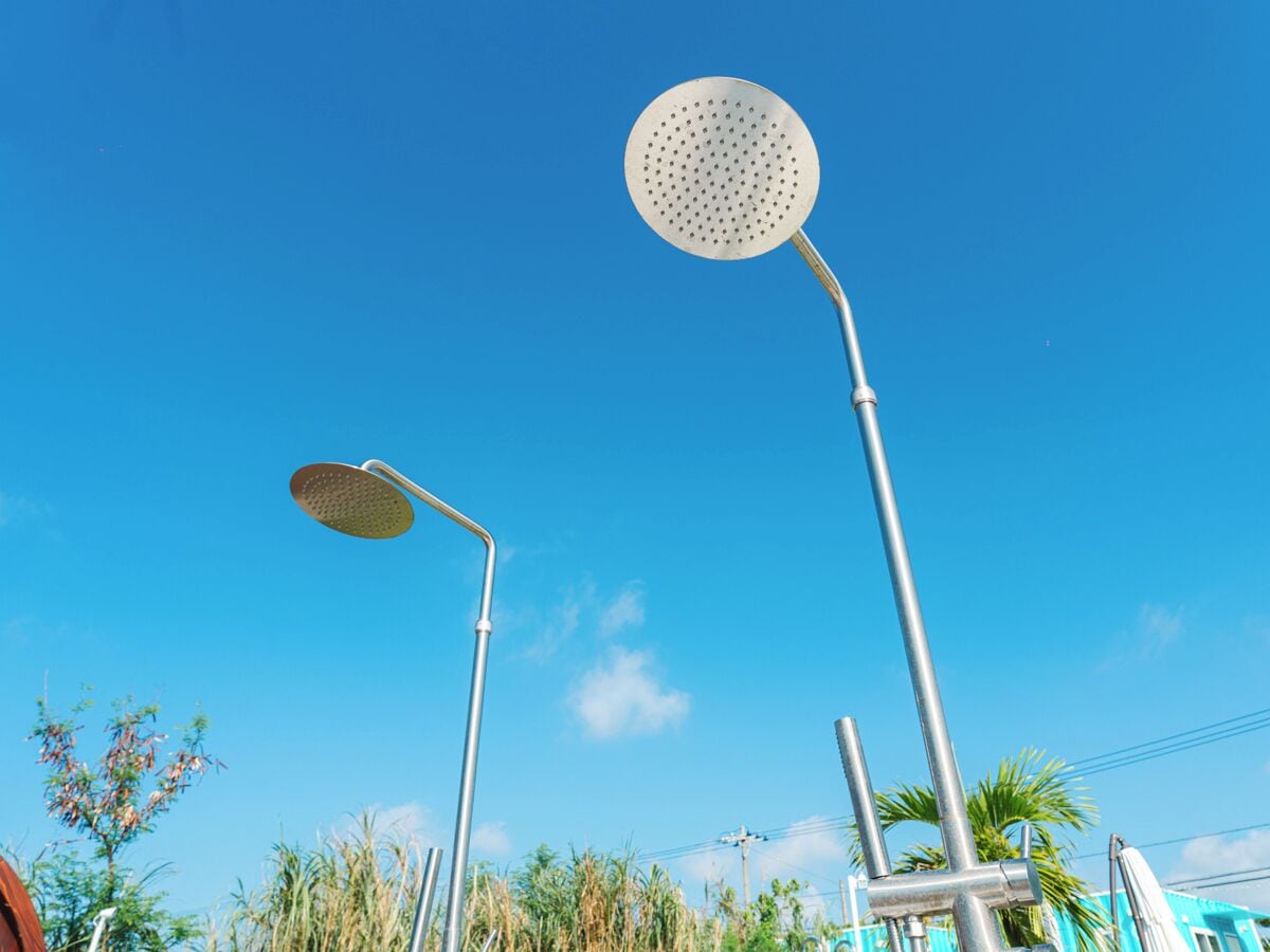 A clear blue sky with two metal structures, one with a circular top and another with a flat top, against a backdrop of greenery and a building.