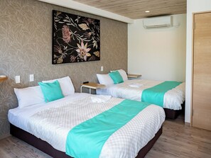 A hotel room with two beds, a wall-mounted air conditioner, and a wooden door. - MIYAKOJIMA Blue Village HOTEL & SAUNA (Miyakojima)