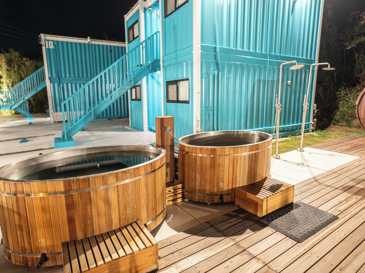 A wooden deck with two hot tubs and a staircase leading to a blue building.