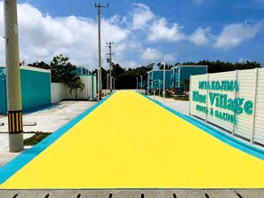 A pathway leading to a building with a sign reading 'Miya Kojima Blue Village Hotel & Sauna'. - MIYAKOJIMA Blue Village HOTEL & SAUNA (Miyakojima)