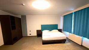 Une chambre d’hôtel avec un lit, une table de chevet, une armoire et une grande fenêtre avec des rideaux.