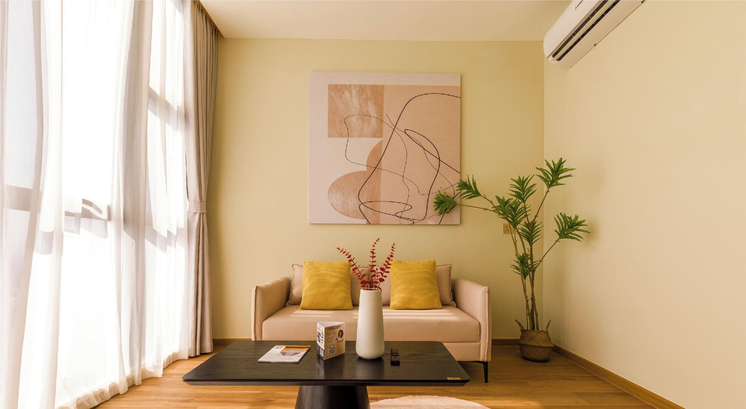 A living room with a sofa, a coffee table, a vase with plants, and a wall-mounted air conditioner.