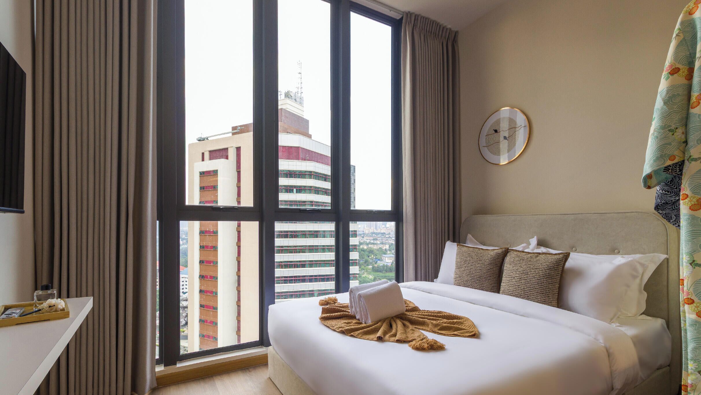 Una habitación de hotel con un ventanal grande, una cama con sábanas blancas, una mesita de noche y un reloj de pared.