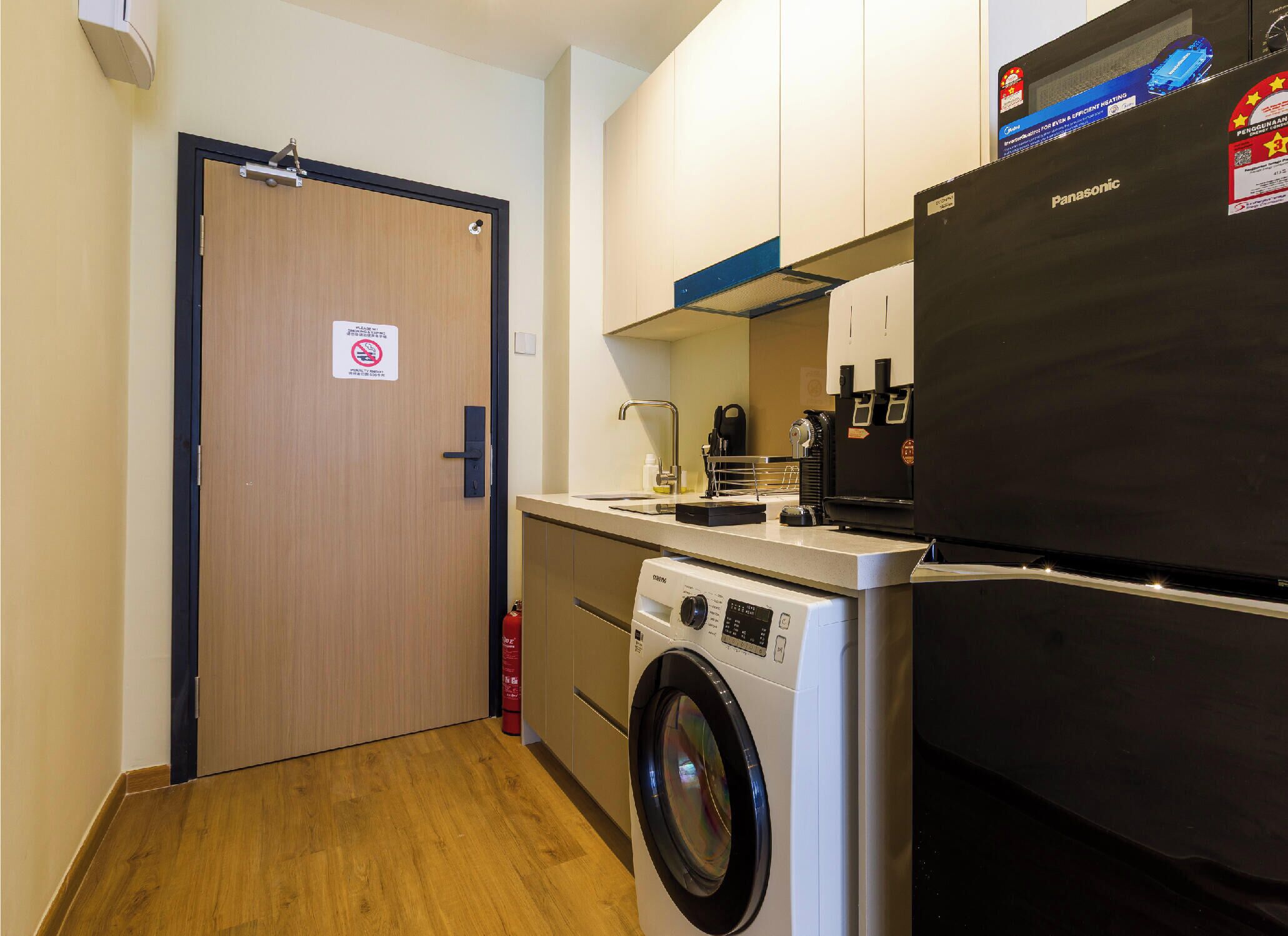 A compact kitchen with a washing machine, a refrigerator, and a coffee machine.