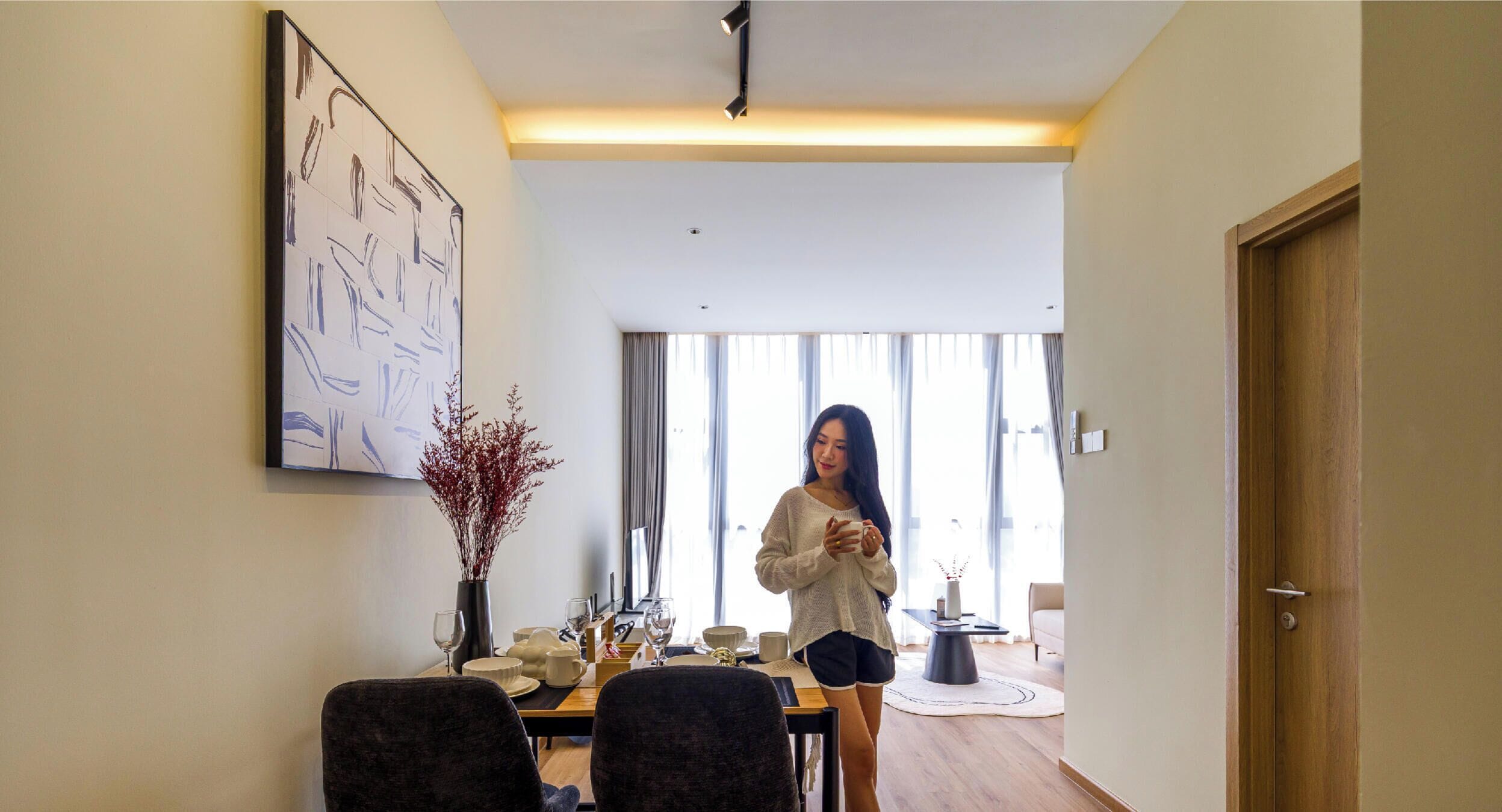 A modern living room with a dining area, a large abstract painting, and a person standing by the window.
