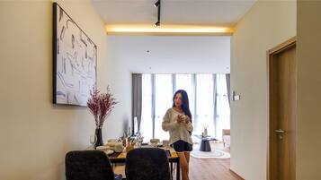 A modern living room with a dining area, a large abstract painting, and a person standing by the window.
