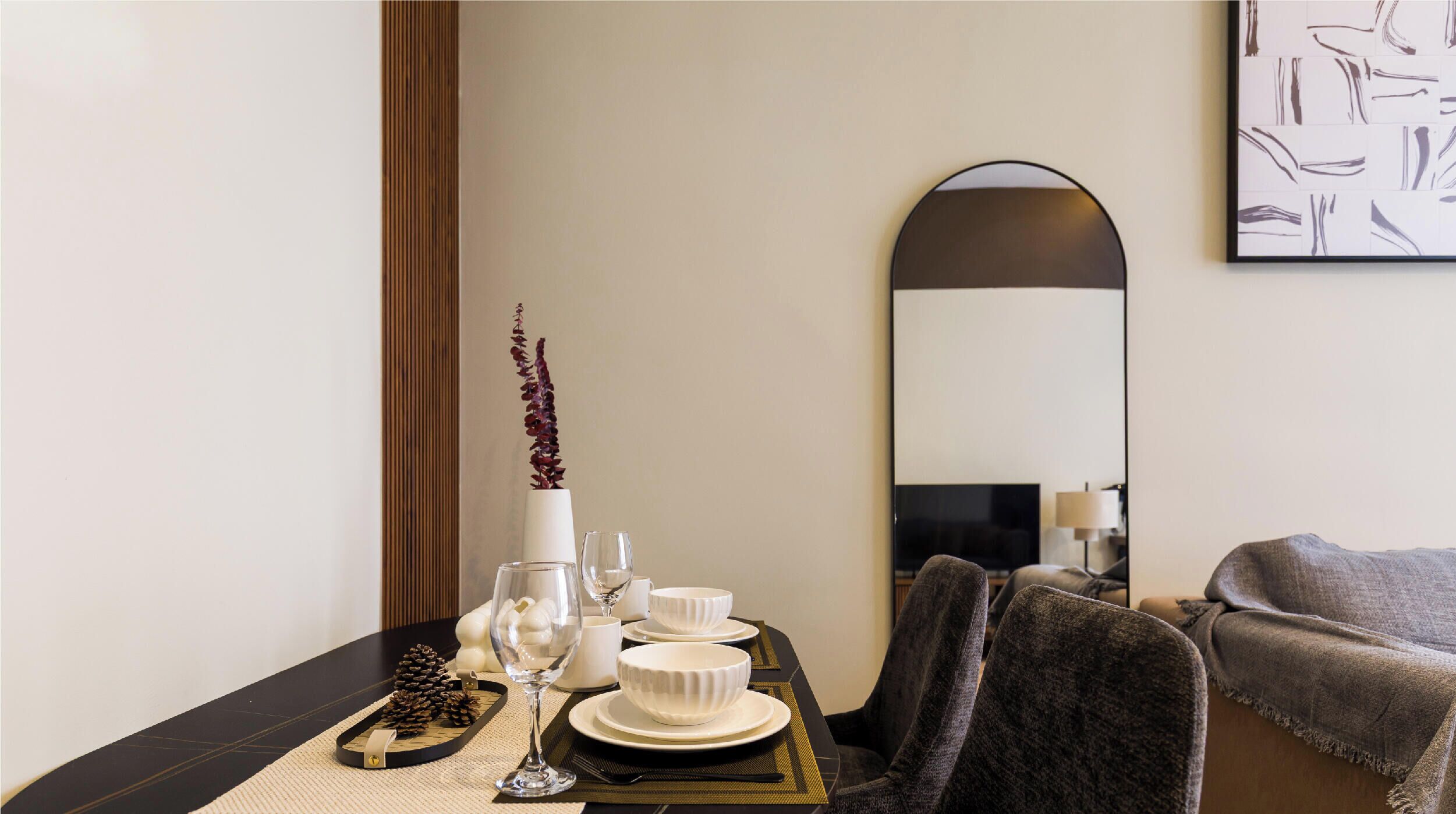 A dining area with a table set for two, a mirror, and a painting on the wall.