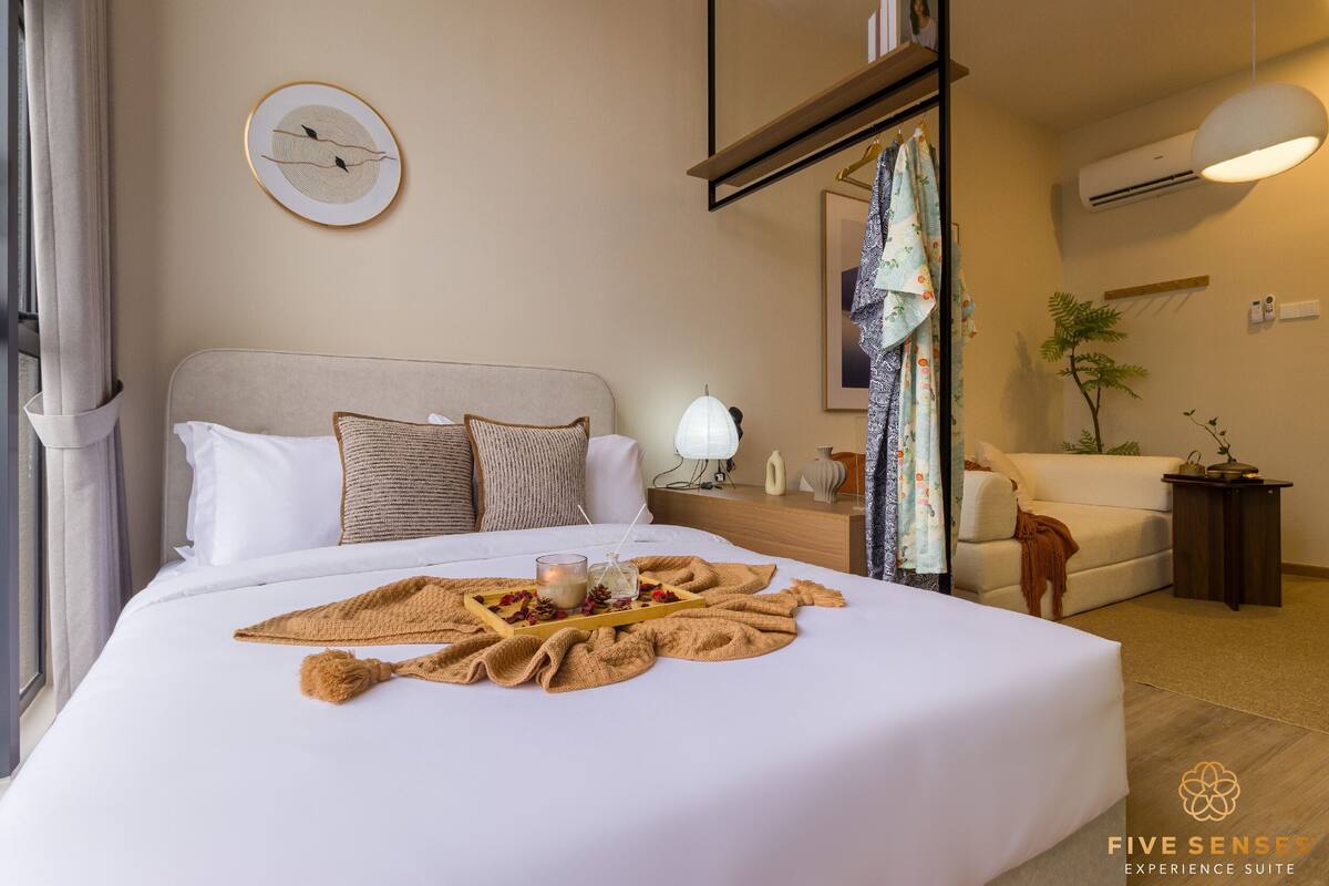 A neatly made bed with a tray of items, a bedside table with a lamp, and a window with curtains.