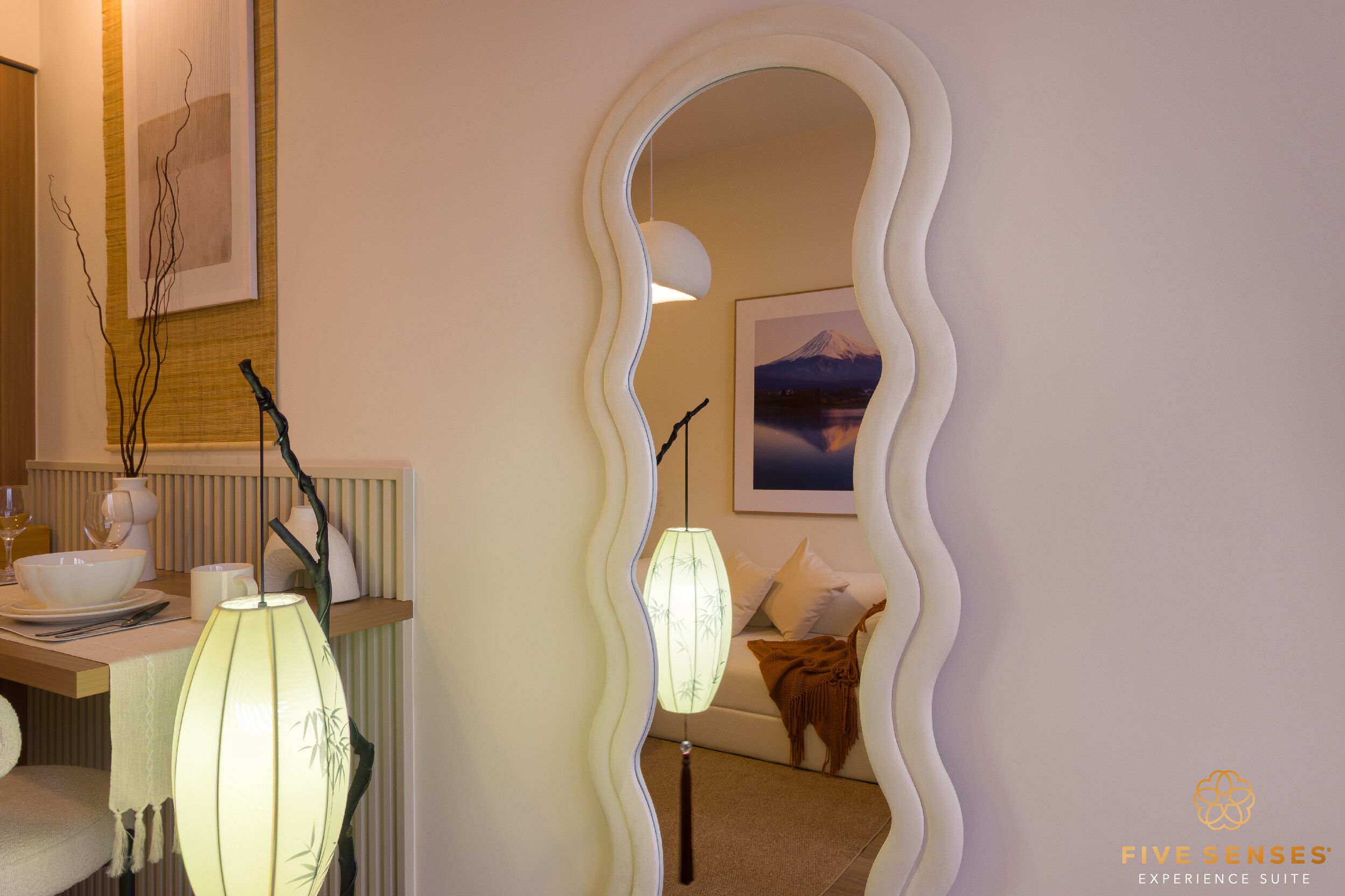 A room with a wavy mirror, a dining table with a vase and a lamp, and a framed picture on the wall.