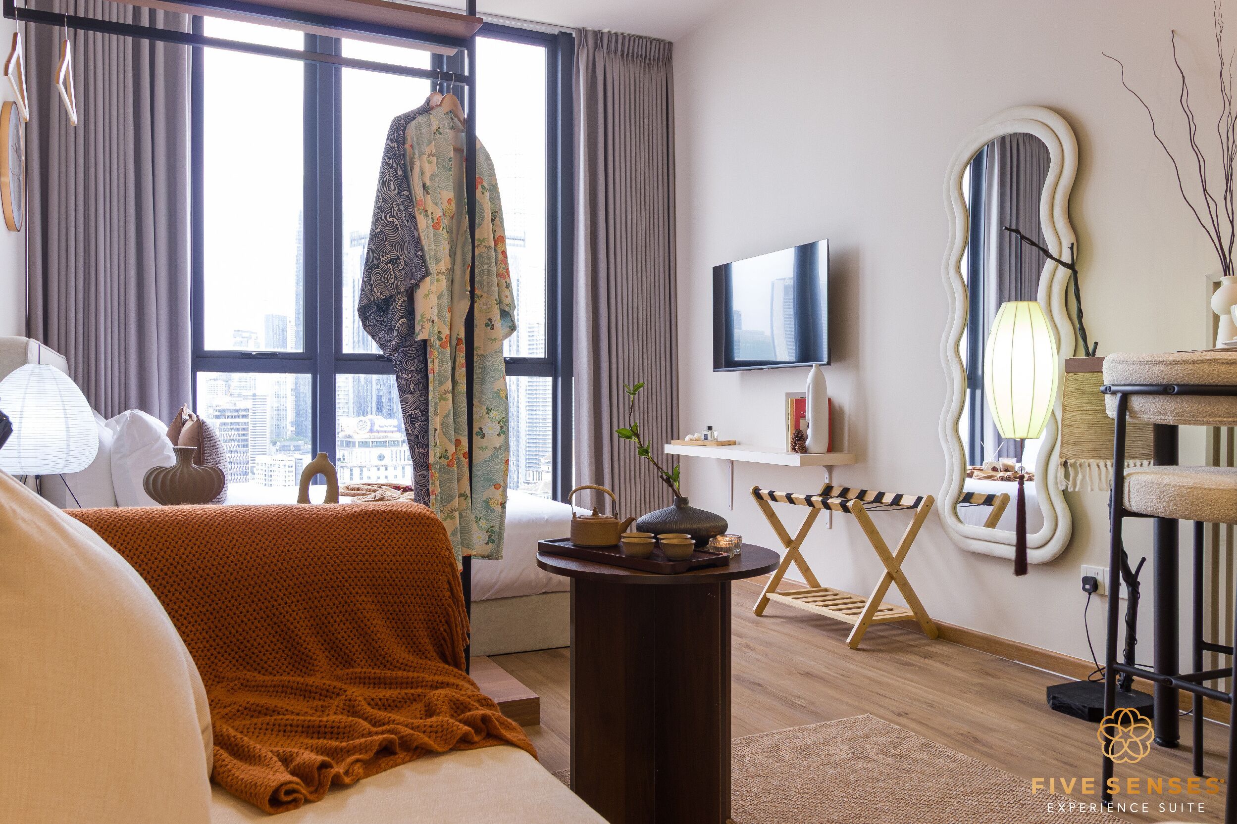 A modern hotel room with a large window, a bed, a TV, a mirror, and a cat tree.