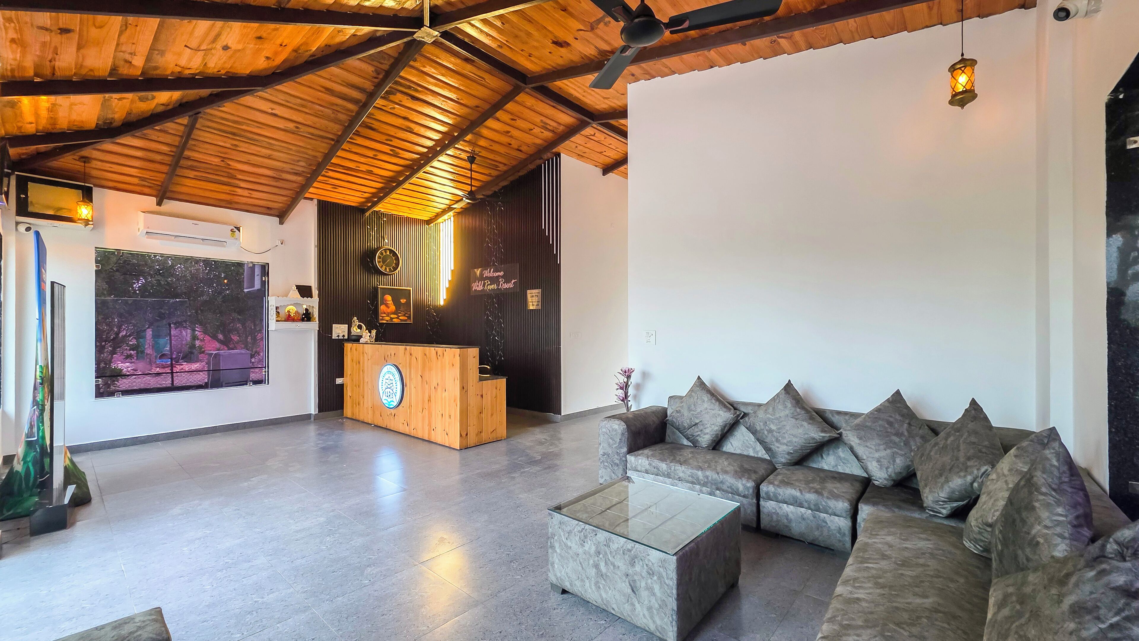 A spacious lobby with a wooden ceiling, a reception desk, a sofa, and a glass coffee table.