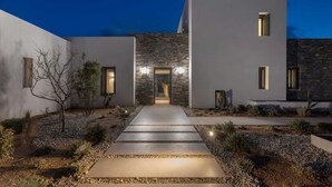 A modern building with a stone facade, a central entrance, and a pathway leading to the entrance. - Celestial II             ., Villa (Paros)