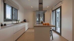 A modern kitchen with a central island, large windows, and a view of the city. - Celestial II             ., Villa (Paros)