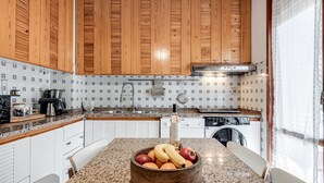 Une cuisine avec des meubles en bois, un plan de travail en granit, un panier de fruits et un lave-vaisselle.