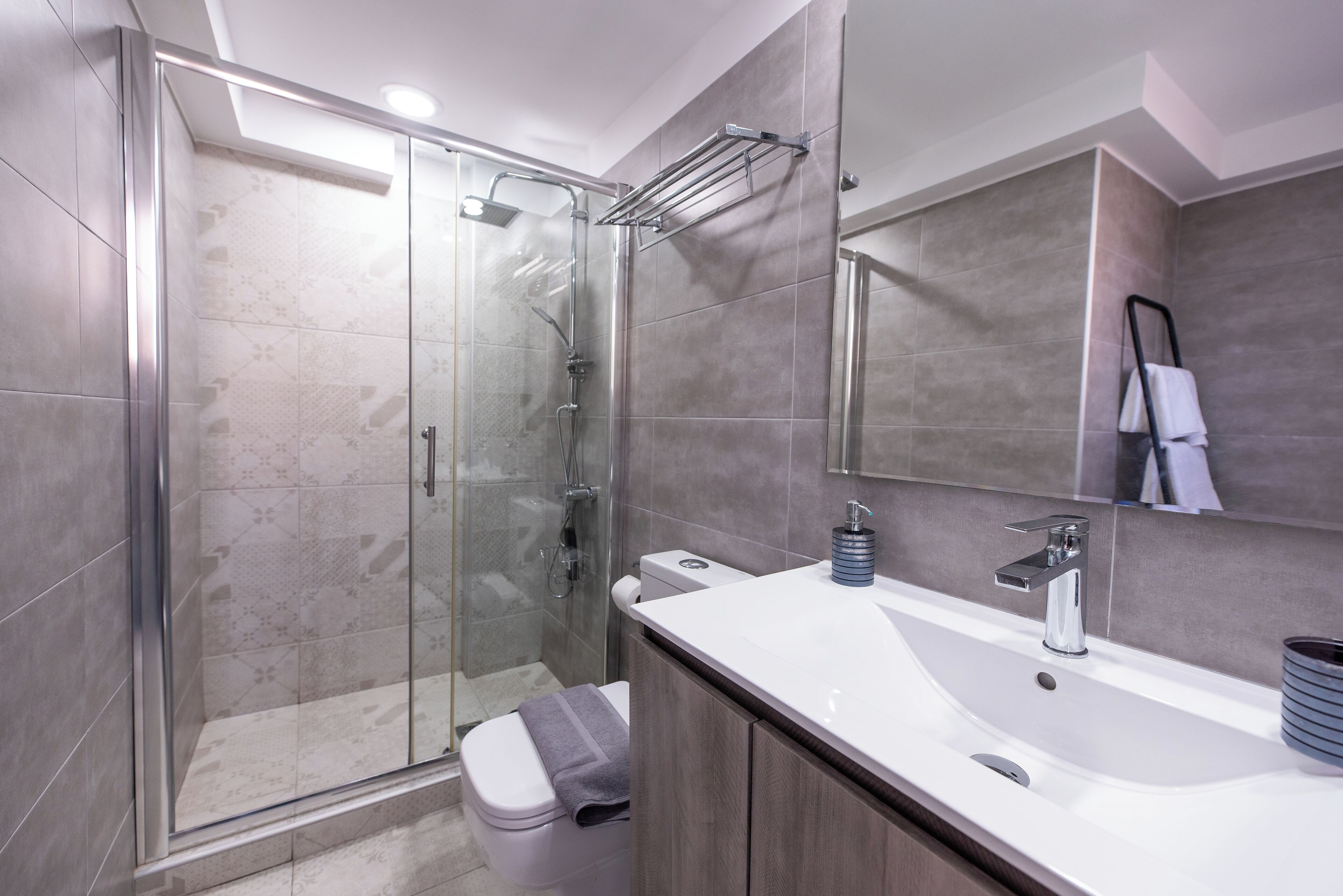 A modern bathroom with a glass shower enclosure, a white sink with a mirror above it, and a towel rack.