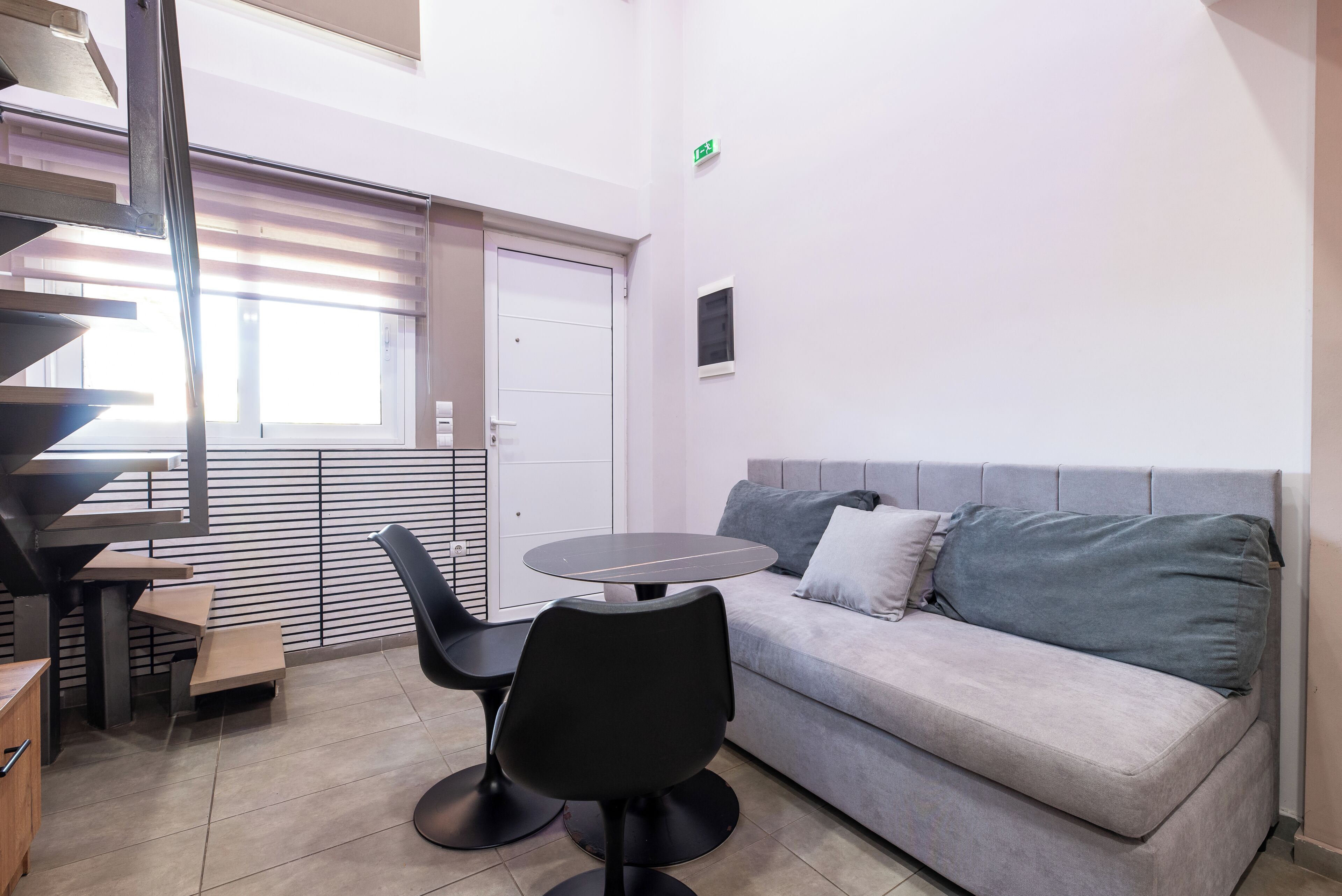 Una habitación moderna con un sofá gris, una mesa redonda y una silla negra.