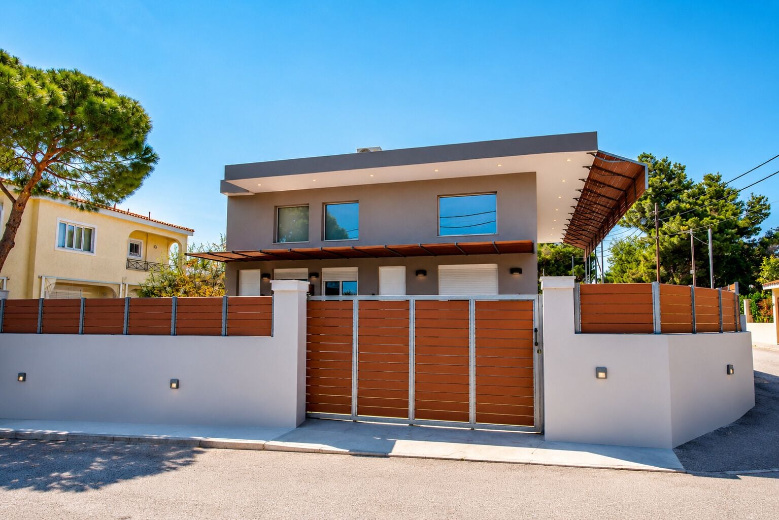 Een modern herenhuis met een hekpoort, een plat dak en een zichtbare garage.