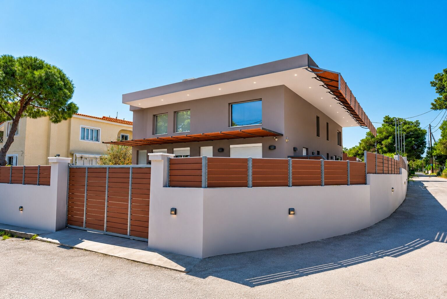 A modern two-story house with a flat roof, a large window, and a gated entrance.