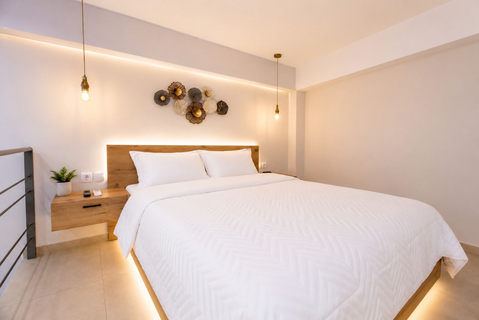 A modern bedroom with a wooden headboard, a bedside table with a plant, and a wall-mounted light fixture.
