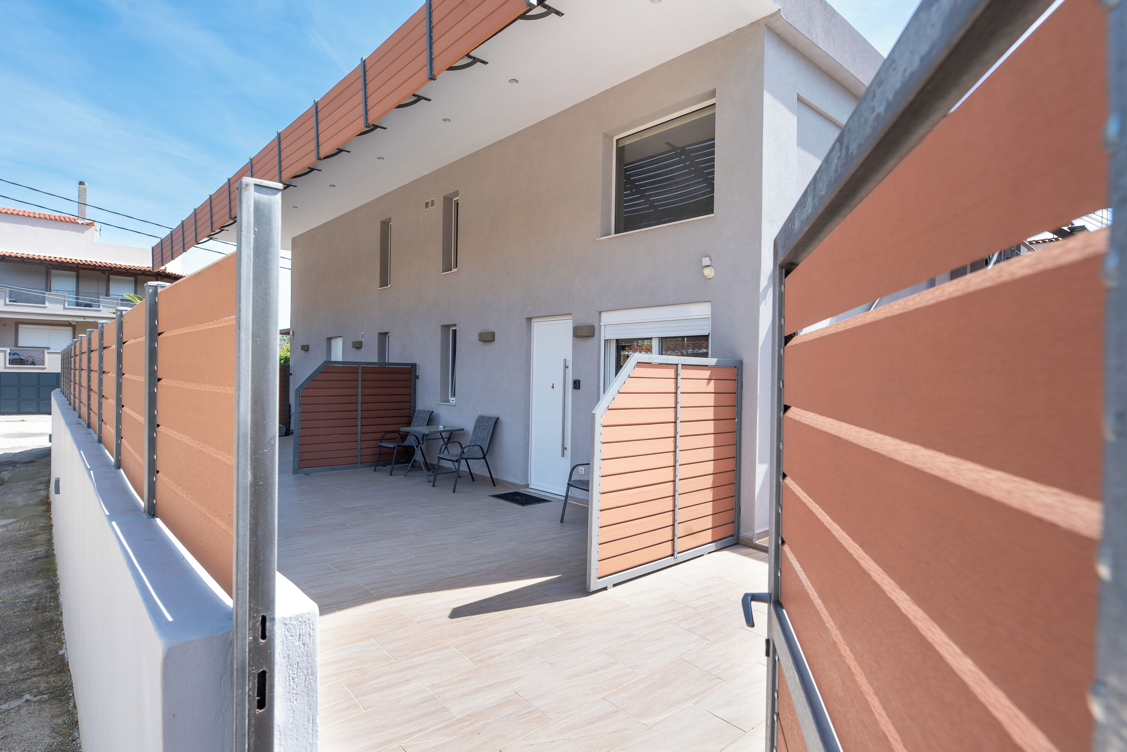 A modern building with a covered outdoor area, a door, and a small table with chairs.