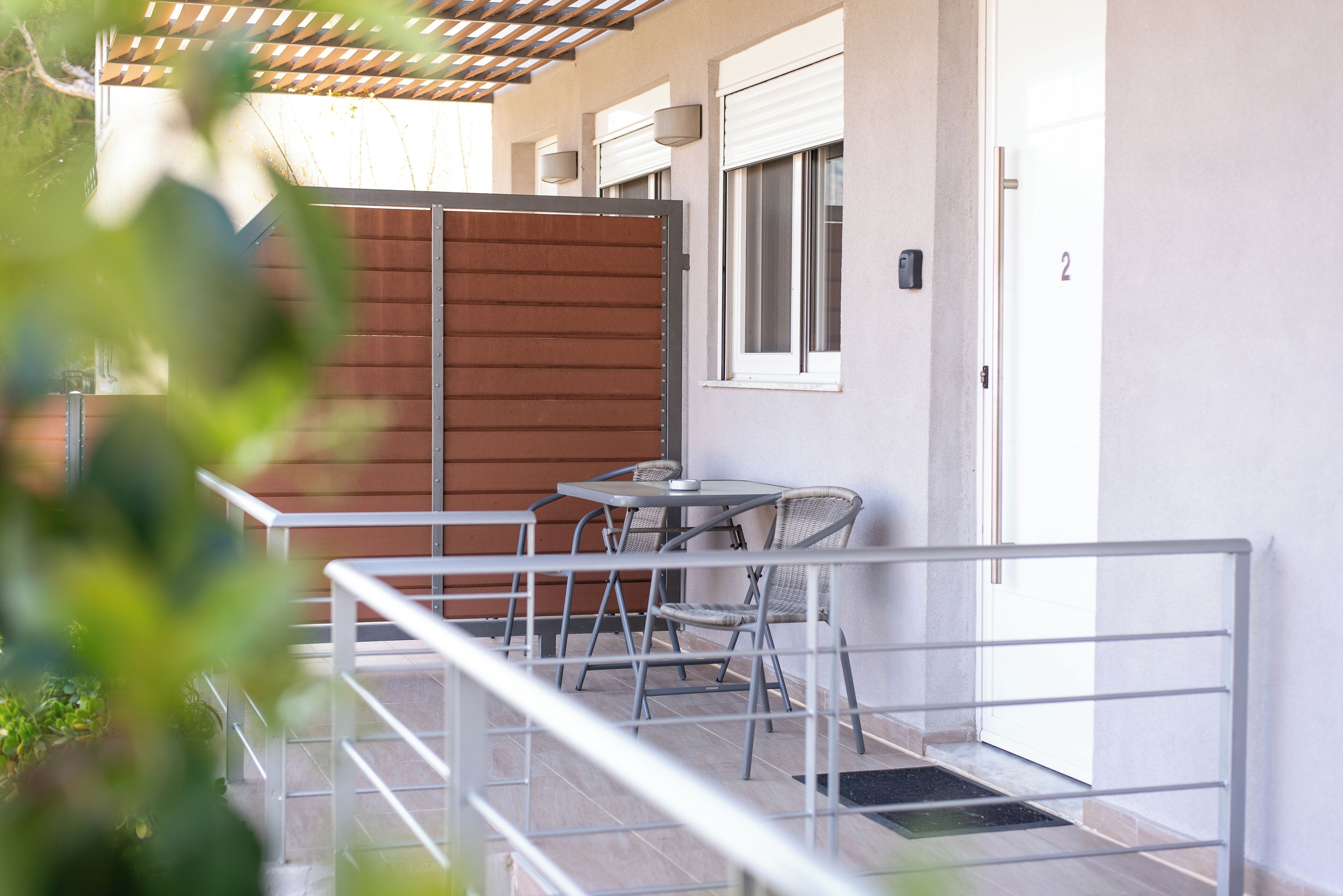 A balcony with a metal railing, a table, and two wicker chairs.