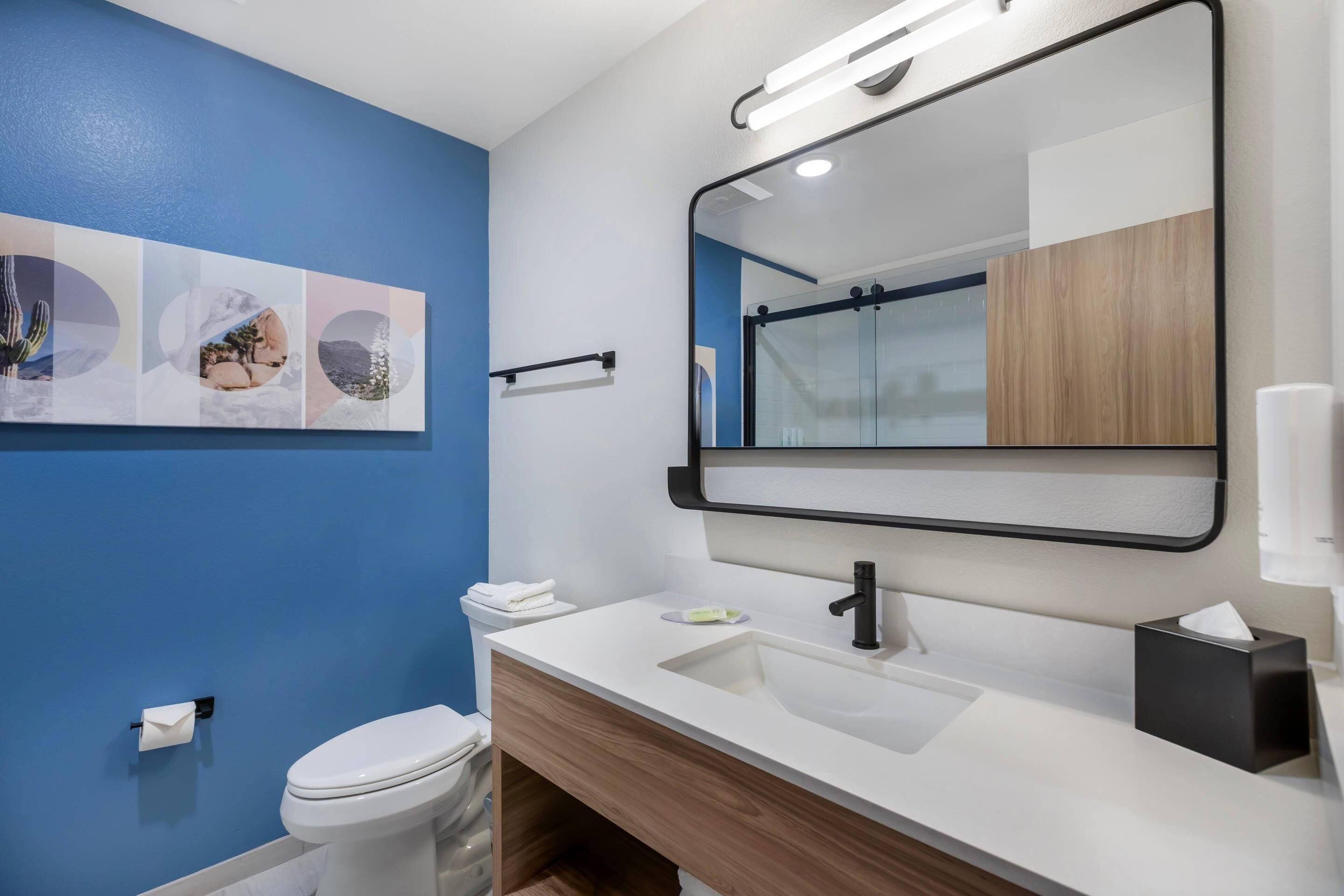 A bathroom with a blue wall, a white toilet, a sink with a mirror, and a towel rack.