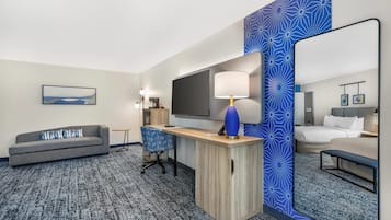 Habitación de hotel con sofá, escritorio, televisor y un espejo grande.