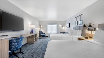 Ein Hotelzimmer mit Flachbildfernseher, Schreibtisch mit Stuhl, zwei Betten, einem Fenster und Wandleuchten.