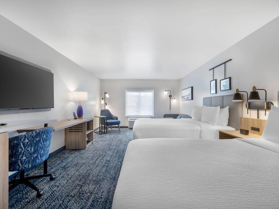 Ein Hotelzimmer mit Flachbildfernseher, Schreibtisch mit Stuhl, zwei Betten, einem Fenster und Wandleuchten.