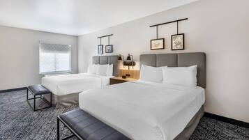 A hotel room with two beds, a bench, a bedside table, and a window with a view.