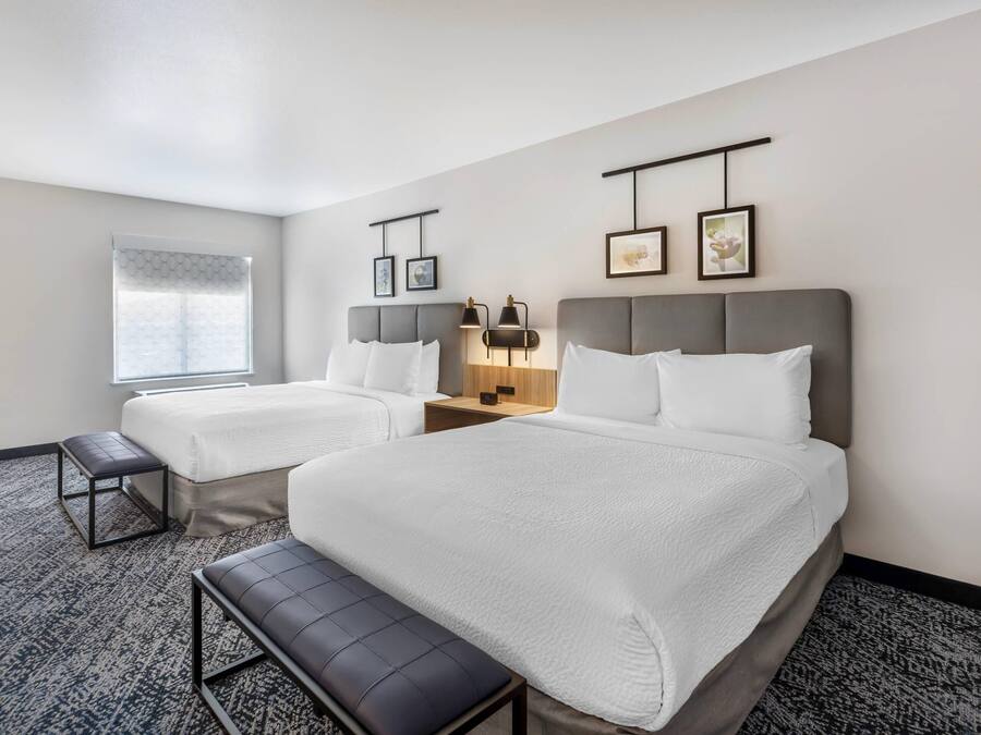 A hotel room with two beds, a bench, a bedside table, and a window with a view.