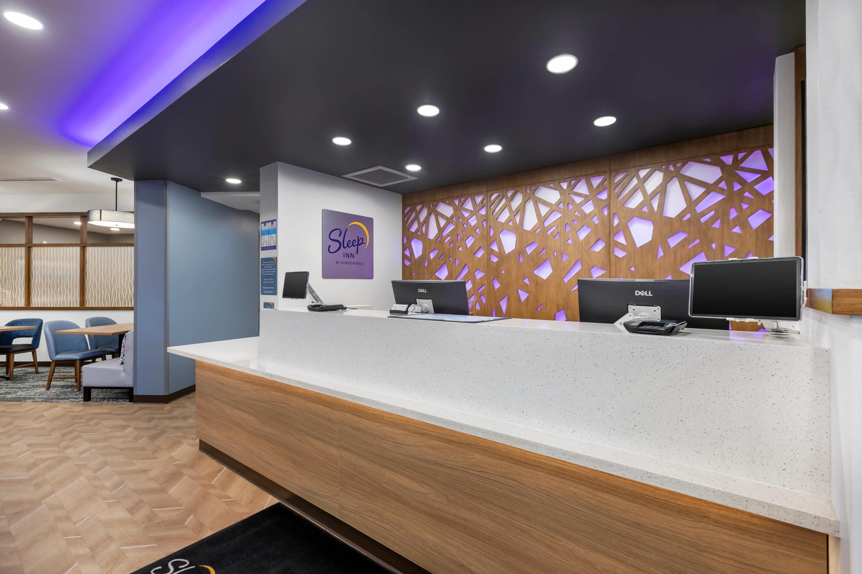 A hotel reception desk with a sign for 'Sleep Inn by Chuck E. Cheese,' a wooden partition with a geometric pattern, and two Dell computers.