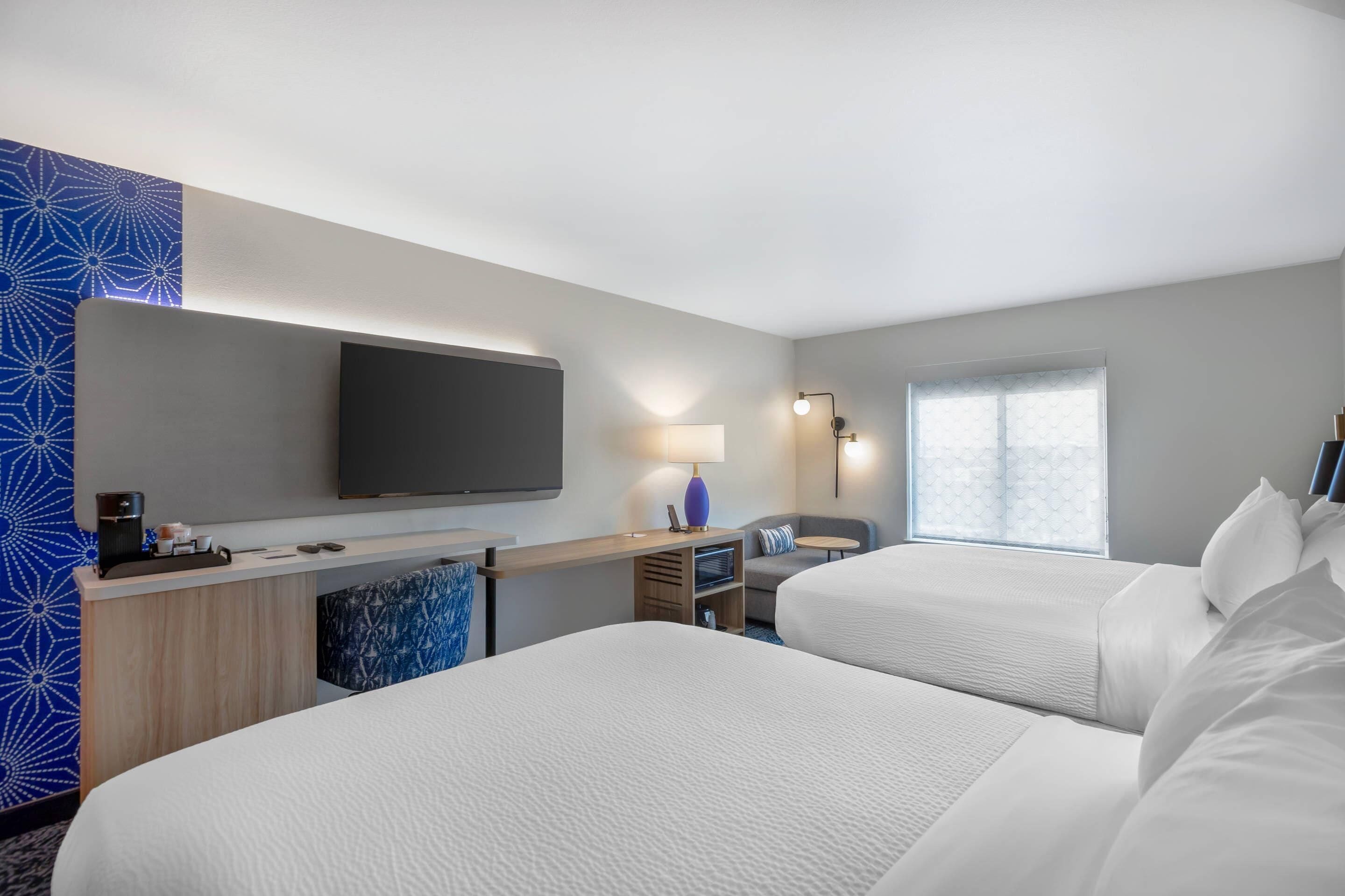 Habitación de hotel con dos camas, un escritorio, un televisor de pantalla plana, una lámpara y una ventana con vistas.
