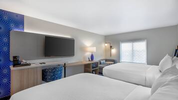 Habitación de hotel con dos camas, un escritorio, un televisor de pantalla plana, una lámpara y una ventana con vistas.