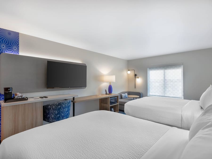 Habitación de hotel con dos camas, un escritorio, un televisor de pantalla plana, una lámpara y una ventana con vistas.