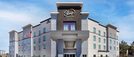 Um hotel Sleep Inn & Suites com design moderno, destacando uma entrada imponente e uma bandeira.