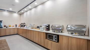 Una cocina moderna con una barra alargada, equipada con cafeteras, microondas y tostadora.