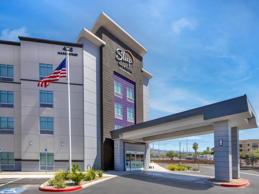 Un hôtel Sleep Inn & Suites au design moderne, facilement reconnaissable grâce à un grand drapeau américain et à une entrée bien visible.